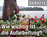 Blumen, Kerzen und eine norwegische Flagge mit der Insel Utöya im Hintergrund