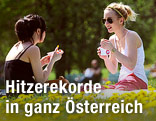 Zwei junge Frauen essen auf einer Wiese Eis