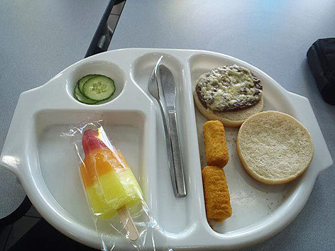 © picturedesk.com/Rex Features Gurkenscheiben, Weißbrot mit Aufstrich, zwei Kroketten, ein Speiseeis und Besteck auf einem Teller