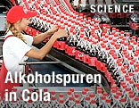 Eine Mitarbeiterin des Produktionszentrums von Coca-Cola am Förderband mit Flaschen