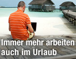 Mann arbeitet am Steg mit Meeresblick auf seinem Laptop