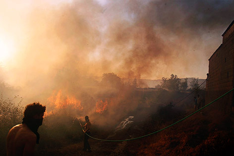 Menschen kämpfen mit einem Gartenschlauch gegen das Feuer