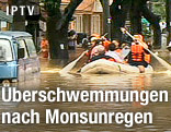 Menschen werden auf einem Schlauchboot durch eine überflutete Straße gefahren