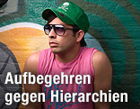 Jugendlicher mit Sonnenbrille und Kappe vor einer Graffiti-Wand