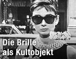 Audrey Hepburn steht im Film "Frückstück bei Tiffanys" mit einer Sonnenbrille vor einem Schaufenster (1961)