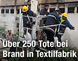 Feuerwehrleute vor dem ausgebrannten Fabriksgeb&auml;ude