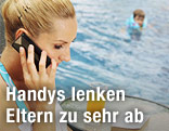 Frau telefoniert am Handy, Kind schwimmt im Swimmingpool im Hintergrund