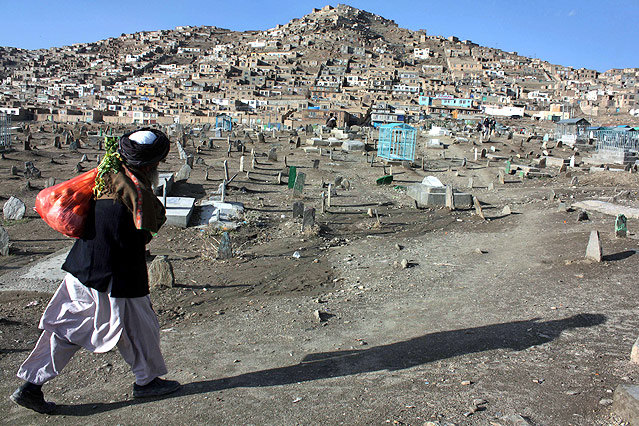 © APA/EPA/S. Sabawoon Ein Mann geht in Kabul vor einem Hügel mit einfachen Häusern an einem Friedhof vorbei