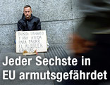 Ein Mann sitzt mit einem Schild auf der Straße und bittet um Geld