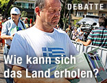 Mann hat auf seinem T-Shirt eine griechische Flagge und trägt eine Kartonschachtel