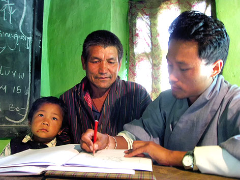 © Thimfilm Ein Beamter in Bhutan schreibt neben einem Mann und einem Kind in ein Heft