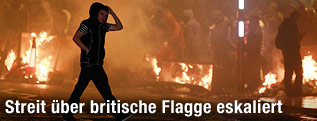 Mann mit Kapuze geht durch ein brennendes Stra&szlig;engebiet