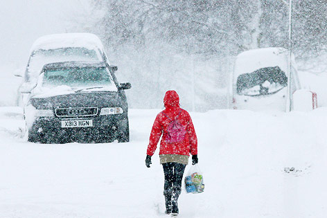 © AP/Scott Heppell Eine Frau mit Kapuze geht vor einem Auto mit britischem Kennzeichen durch starken Schneefall