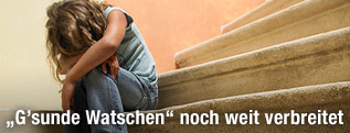 Kind sitzt zusammengekauert auf der Treppe