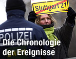 Eine Demontrantin hält ein Schild mit durchgstrichenem "Stuttgart 21"-Schriftzug und steht vor einem Polizisten