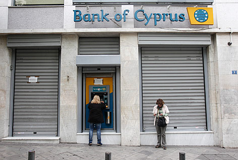 Eine Frau behebt Geld bei einem Bankomat einer Filiale der Bank of Cyprus mit heruntergelassenen Rollläden