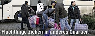 Fl&uuml;chtlinge beladen einen Bus f&uuml;r den Umzug ins neue Quartier