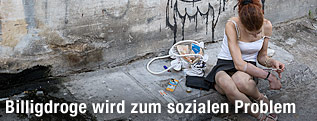 Drogenabhängige Frau sitzt auf Gehsteig
