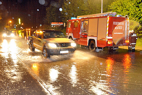 © APA/Manfred Fesl Ein Auto fährt auf einer überfluteten Straße an einem Feuerwehrauto vorbei