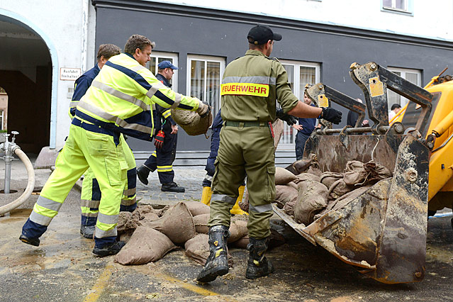 Feuerwehrmänner werfen Sandsäcke in Baggerschaufel