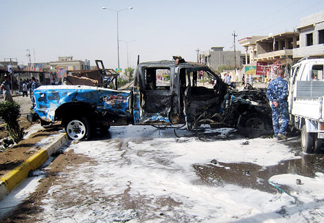 Polizist nahe eines durch eine Autombombe ausgebranntes Autowracks in Kirkuk