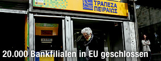 Alte Frau vor einer Filiale der Piraeus Bank in Athen