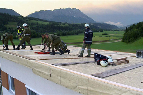 Feuermänner fixieren eine Plane auf einem Mehrparteienhaus nach dem heftigen Unwetter im Bezirk Liezen