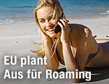 Frau liegt auf dem Strand und telefoniert mit Handy
