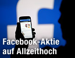 Mann hält Handy vor Facebook-Logo