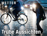 Eine Radfahrerin und eine Fußgängerin mit Schirm auf einer Straße im Regen