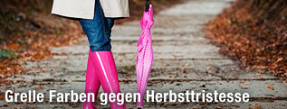 Frau in Regenmantel mit rosa Schirm und rosa Gummistiefel