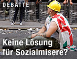 Ein Arbeiter mit Helm und umgehängter Fahne sitzt auf der Straße