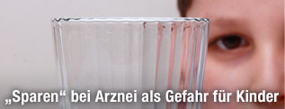 Kind hinter einem Wasserglas mit Tabletten davor