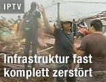 Mann mit Helm vor zerstörten Häusern
