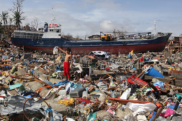 © APA/EPA/Francis R. Malasig Ein Bub steht in Unrat vor einem gestrandeten Schiff