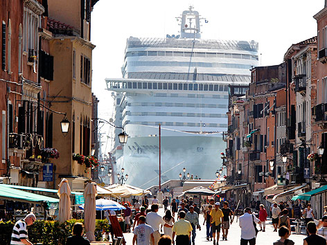 Touristen marschieren vor einem riesigen Kreuzfahrtschiff in der Lagune durch Venedig