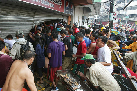 © APA/AP/Aaron Favila Menschen zerstören in der Stadt Tacloban die Rollläden eines Geschäfts um es zu plündern