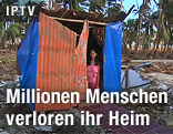 Frau steht in behelfsmäßig errichteter Wellblechhütte
