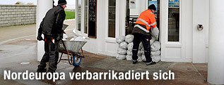 Zwei Männer türmen Sandsäcke auf