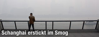 Ein Mann steht vor der durch Smog komplett verdeckten Skyline von Schanghai