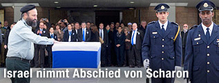 Ein Rabbi legt seine Hand auf Scharons Sarg
