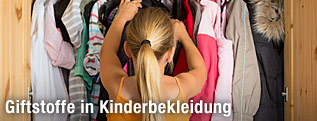 Ein Mädchen greift nach einem Kleidungsstück im Kleiderkasten