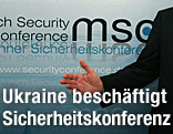 Hand vor einer Wand mit dem Logo der Sicherheitskonerenz