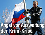 Zwei Männer hissen die russische Flagge bei einem besetzten ukrainischen Militärstützpunkt auf der Krim