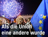 Personen neben einer EU-Flagge blicken auf ein Feuerwerk