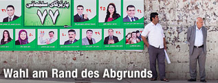 Zwei Männer stehen vor irakischen Wahlplakaten
