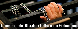 Hand in Ketten hinter einem Gitter