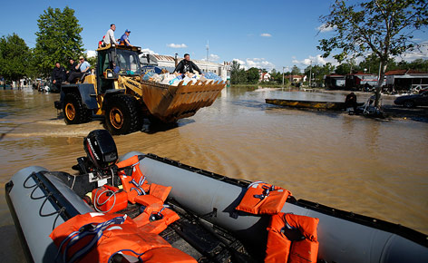 © APA/AP/Darko Vojinovic Männer fahren auf einem Bulldozer durch überflutetes Gebiet