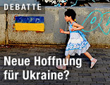 Ein Mädchen läuft an einer Wand mit aufgemalter ukrainischer Flagge vorbei