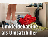 Beine einer weiblichen Person neben Kleidungsstücken in einer Umkleidekabine